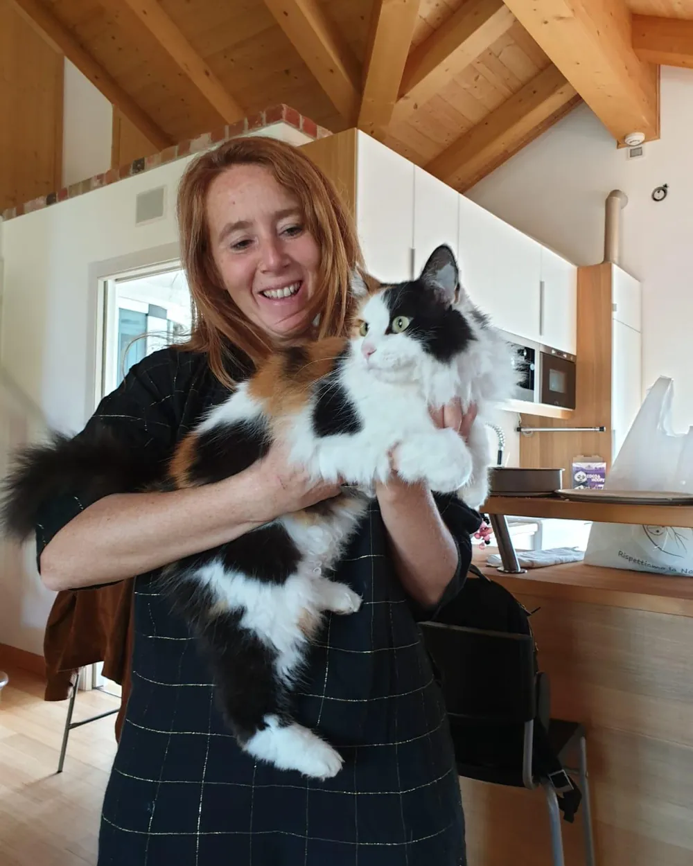 Una delle titolari di Ginger Guest sorride in un soggiorno con travi di legno a vista, tenendo in braccio il suo gatto tricolore